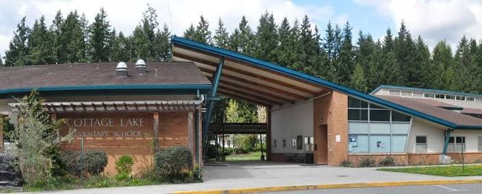 Front entrance of Cottage Lake Elementary, with its brick sign and blue-trimmed roofline against tall evergreens